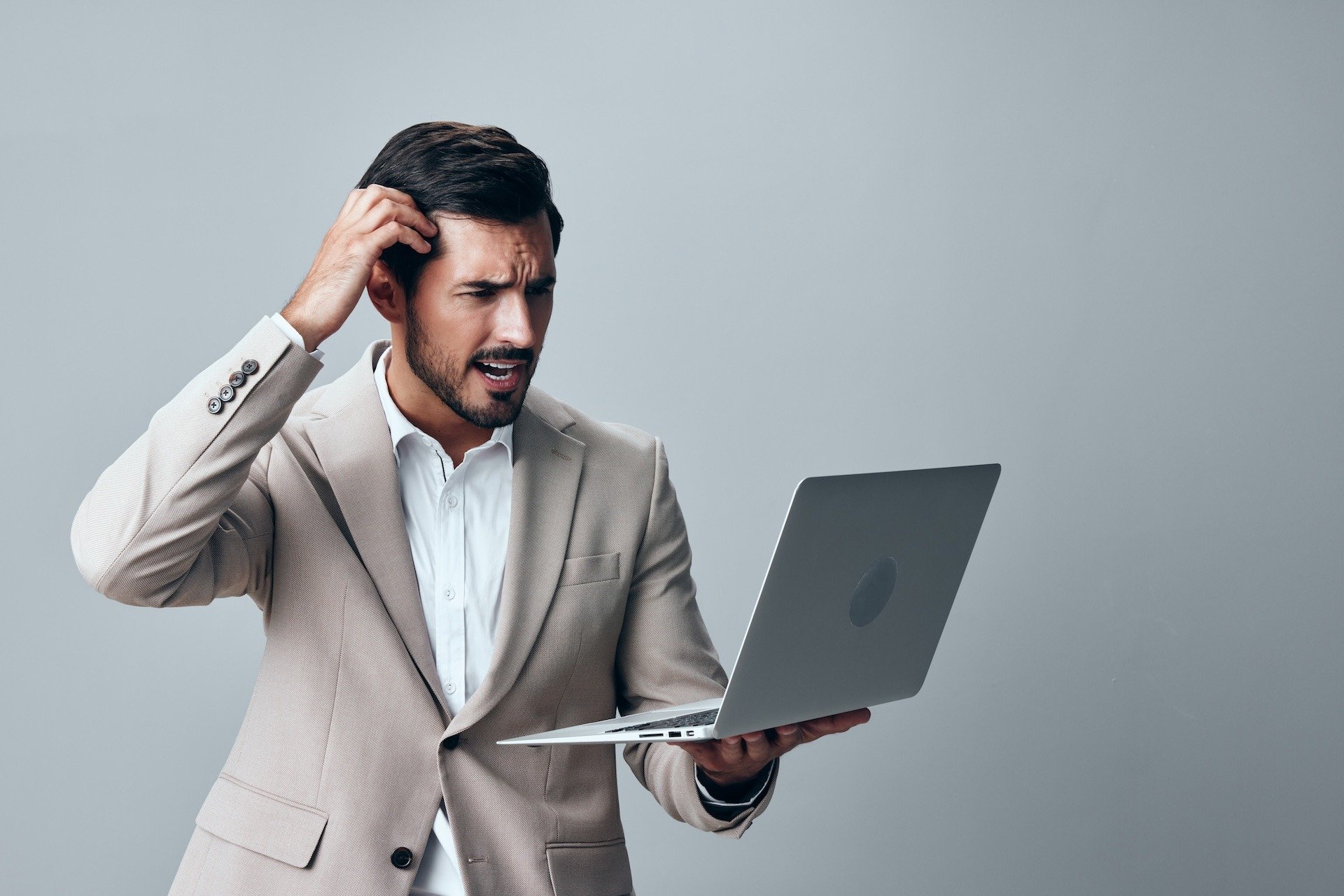 Image of a frustrated businessman looking at the faulty laptop he is holding in his hand