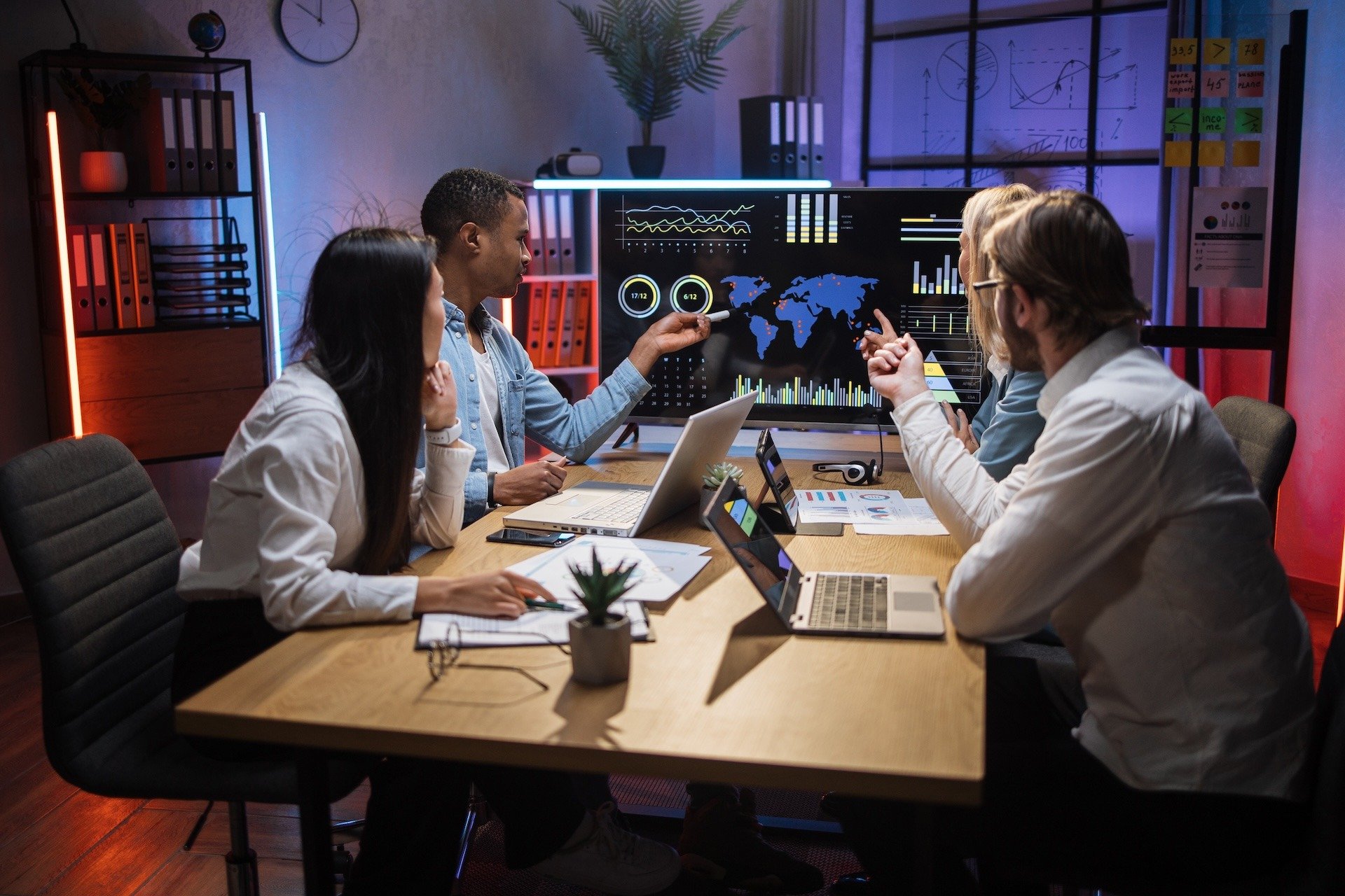 Image shows a team of analysts studying IoT data from a cross the globe on a TV in a conference room